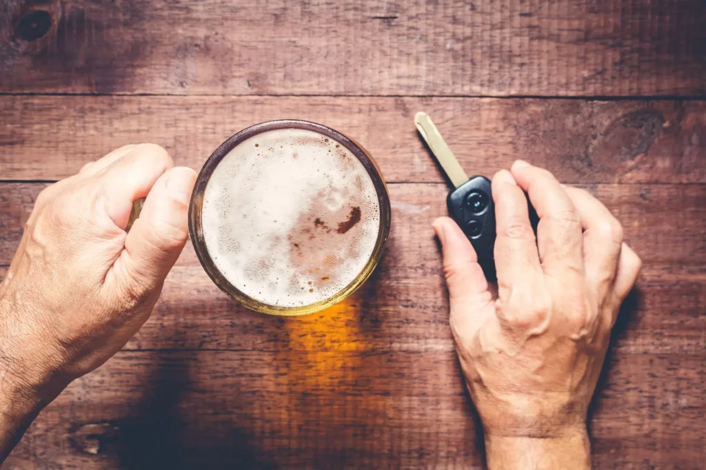 Close-up of a hand holding a glass of beer and car keys