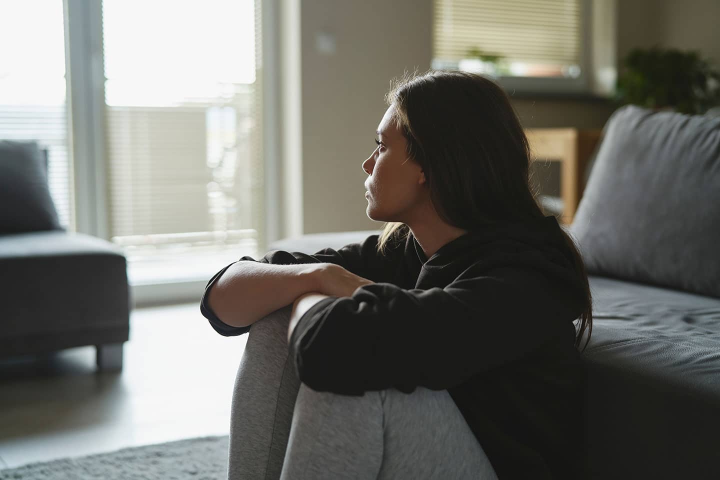 Sad Woman Sitting on the Floor & Looking at the Window | Domestic Abuse Lawyer​​ | Wegman & Levin